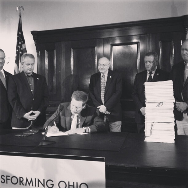 Governor Kasich signs anti-woman budget into law flanked by men.