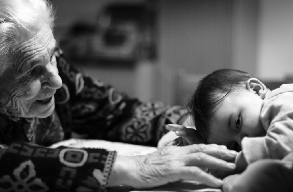 A black and white photo of an older woman reaches out to touch a baby